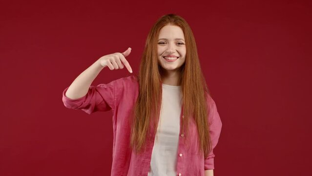 Happy woman pointing down to advertising area. Red background. Young lady asking to click to subscribe below. Copy space for your commercial idea, promotional content.