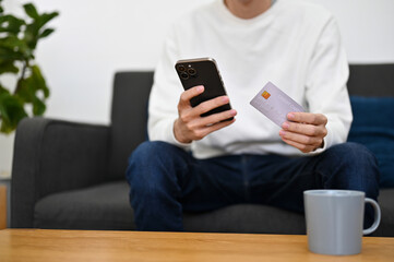 A man is on the sofa, holding a credit card and smartphone. cropped image