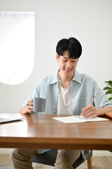 Handsome young Asian male college student sipping coffee while focusing on his homework