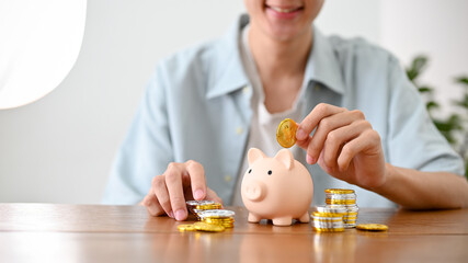 Happy Asian man inserts coins into a piggy bank, saving money for his future plans. cropped shot