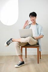 Handsome and joyful Asian man waving his hand to greet his friends via video call on a laptop.
