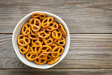 A bowl full of mini pretzels with salt on wooden background, top view, copy space.