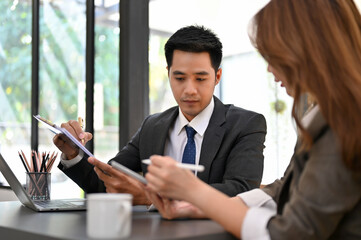 Professional Asian businessman focusing on analyzing financial sales data with his assistant