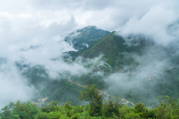 Elevated view of a green mountain valley with low clouds and narrow winding tracks near Sapa in Vietnam
