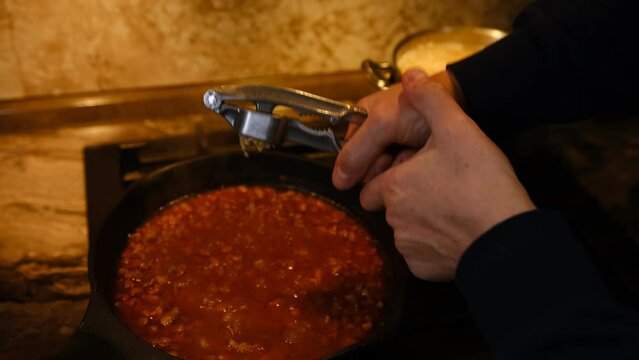 man add garlic in homemade bolognese sauce made of fresh tomato, onion, carrot and mincemeat in a pan.