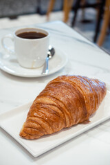 French croissant on white marble table with a cup of black coffee.
