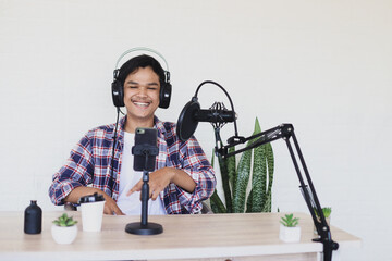 Cheerful young Asian is smiling during shooting vlog using smartphone and podcast broadcasting...