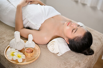 Obraz na płótnie Canvas Beautiful and calm Asian woman lying on massage table with eyes closed, relaxing in spa salon.