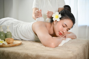 Fototapeta na wymiar Beautiful Asian woman relaxing in spa salon, getting body massage with spa herbal balls