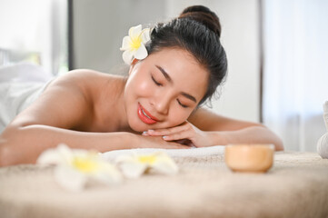 Obraz na płótnie Canvas Beautiful, calm Asian woman lying on massage table with eyes closed in beauty spa salon.