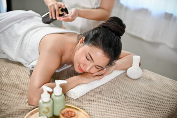 Obraz na płótnie Canvas Charming Asian woman lying in massage table with eyes closed, getting body massage oil on her back