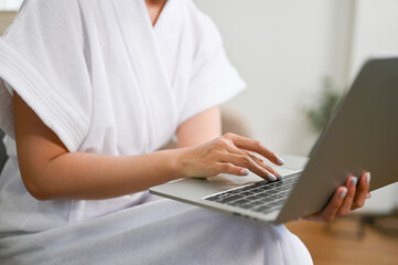 Naklejka premium cropped images, A female in bathrobe using laptop, typing on keyboard, work from home.