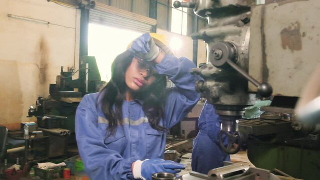 African American female industrial worker in protective and safety uniform and hardhat is tired with works at metalwork machines in manufacturing factory. Professional production engineer occupation.