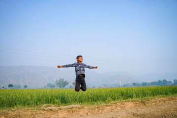 Indian little boy spreading hand and jumping at agriculture field.