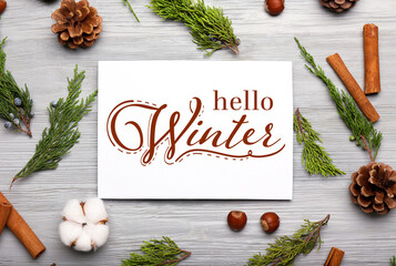 Composition with natural decor and card with text HELLO WINTER on grey wooden background