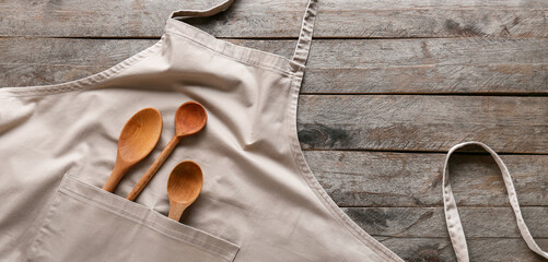 Clean apron and spoons on wooden background