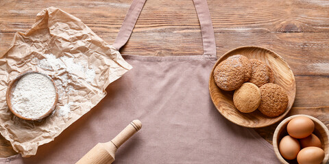 Clean apron, rolling pin, eggs, flour and cookies on wooden background, top view
