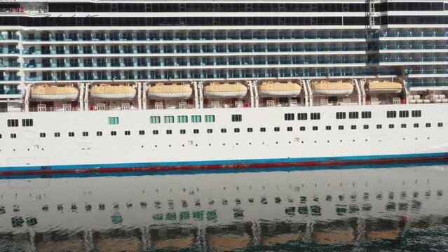 Cruise ship - balconies on the decks, lifeboats and portholes, on the port or starboard side of a luxury boat, including the reflection on the surface of calm sea water.