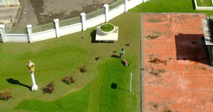 a man mowing the grass with a push mower on a hot sunny day located in aceh