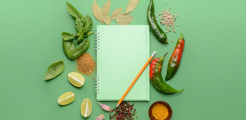 Empty notebook with different spices and pencil on green background