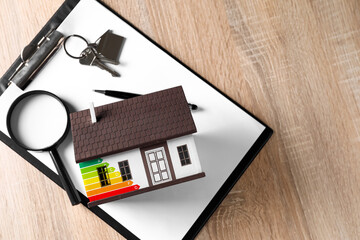 Model of house with key, magnifier and clipboard on wooden background. Concept of energy efficiency