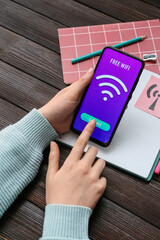 Woman holding mobile phone and connecting to free WiFi zone on wooden background