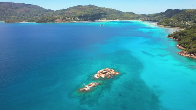 Flying drone near the shore, passing over rcoks, turquoise water, calm sea of anse la mouche beach on Mahe island