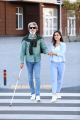 Young woman helping senior blind man to cross road in city