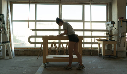 a carpenter girl stands at a workbench at a workbench and grinds a wood blank