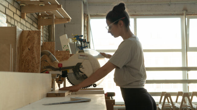 girl carpenter cuts a board on a miter saw - Powered by Adobe