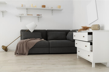 Interior of messy living room with black sofa, standard lamp and drawers