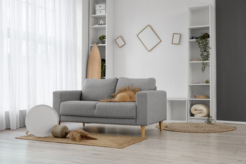 Interior of messy living room with grey sofa, shelving units and surfboard