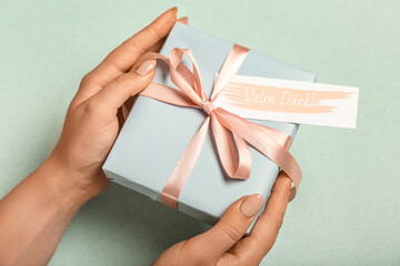Woman holding gift box with card on color background, closeup