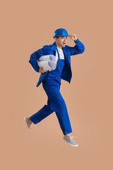 Young male worker with house plans jumping on beige background