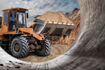 Fototapeta premium The excavator backfills the pit with the front bucket. Moves soil around the construction site. Close-up. Heavy construction equipment.