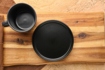 Wooden board with black plate, cup and brown napkin on grunge beige background