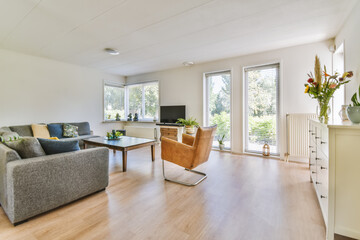 a living room with wood flooring and white walls, including a grey sofa set in the center of the...