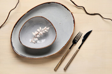 Plate with bowl, floral decor and cutlery on beige background