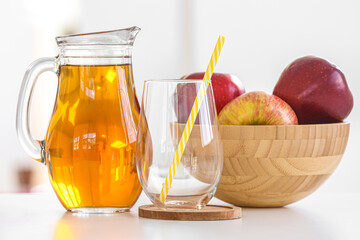 Jug of fresh apple juice, glass and fruits on table in kitchen