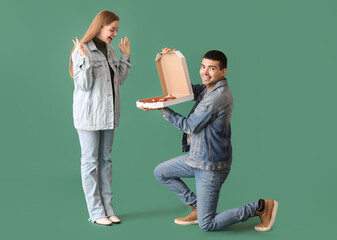 Happy young couple with fresh pizza on green background. Creative marriage proposal - obrazy, fototapety, plakaty