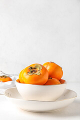 Bowl of ripe persimmons on light background
