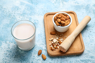 Glass of almond milk, wooden board with nuts and masher on color background