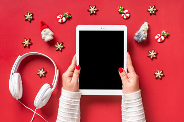 top view female hands holding tablet with black digital screen, Christmas decor, headphones on red table Flat lay Greeting electronic card, book, podcast, music Merry Christmas and Happy New Year - 556391585