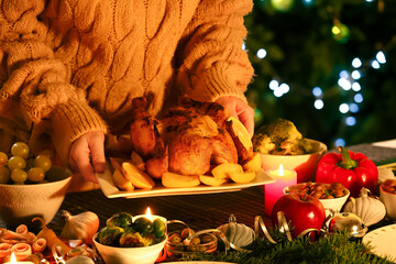 Woman with plate of Christmas chicken near table at home, closeup
