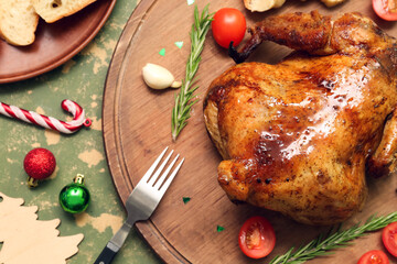 Wooden board with tasty baked chicken and Christmas decorations on color background, closeup