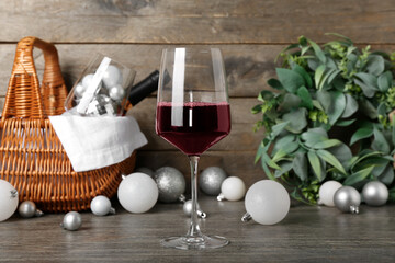 Glass of wine with white Christmas balls on wooden table, closeup