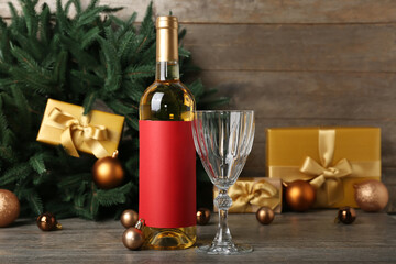 Bottle of wine with glass and golden Christmas balls on wooden table, closeup