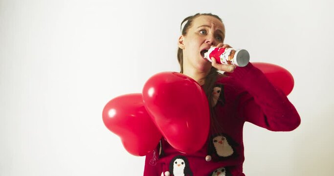 Woman with red hearts around her neck fills her mouth with whipped cream spray. White background. Valentine's Day melancholy