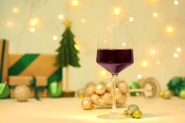 Glass of red wine with Christmas balls on light table, closeup