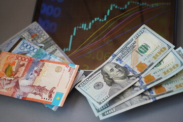 Almaty, Kazakhstan - 10.04.2022 : Stock charts on the tablet and tenge and dollar banknotes on the table.